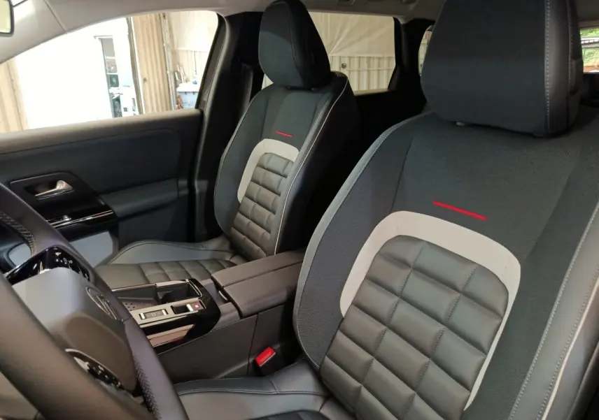 Vue intérieure rapprochée des sièges avant gris foncé et noirs avec surpiqûres rouges de la Citroën C5 Hybride 2026.