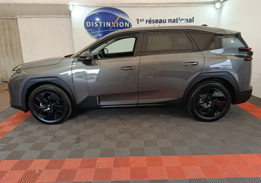 Vue de profil côté gauche d'un Citroën C5 Hybride gris foncé avec jantes noires dans un showroom.
