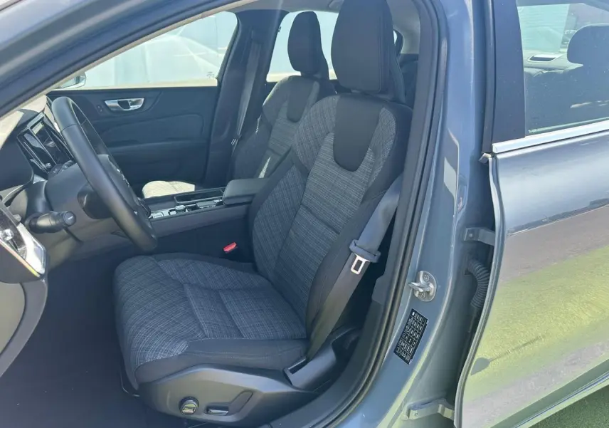 Intérieur avant droit d'une Volvo S60 2024 Thunder Grey Metal, siège tissu gris à motifs et volant noir.
