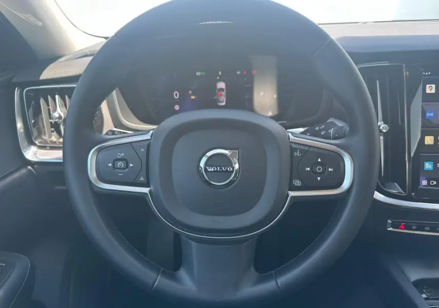 Volant en simili-cuir noir avec commandes intégrées et logo Volvo au centre du tableau de bord d'une S60 2024.