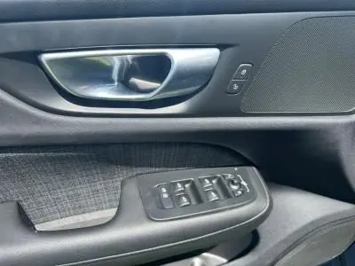 Gros plan sur la poignée intérieure et les commandes des vitres côté conducteur d'une Volvo S60 Thunder Grey 2024.