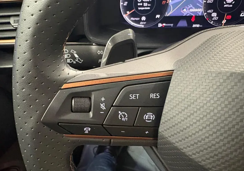 Gros plan sur les commandes à gauche du volant perforé du CUPRA Formentor gris magnétique, avec tableau de bord numérique en arrière-plan.