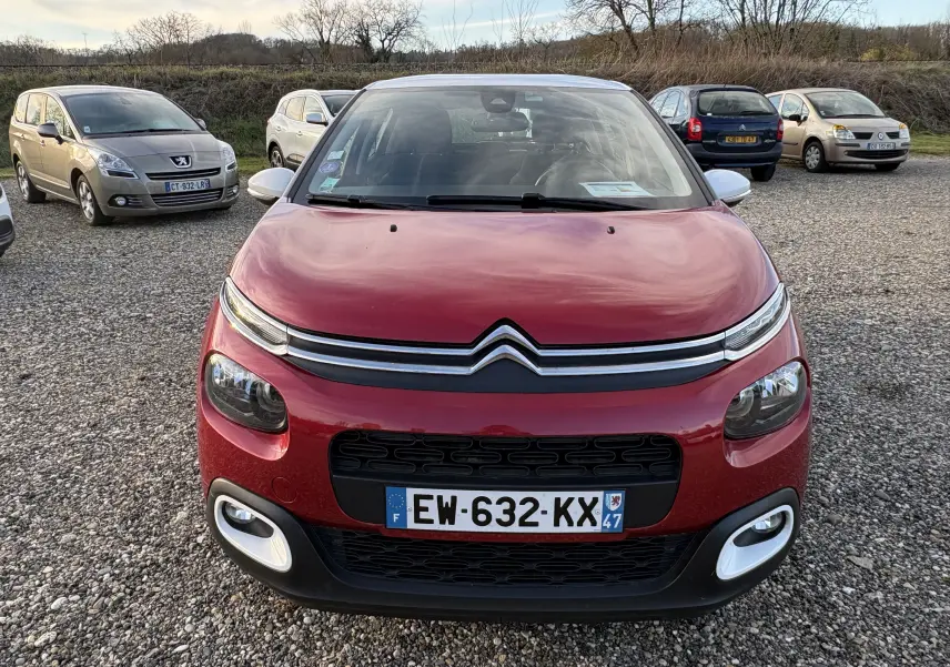 Vue avant d'une Citroën C3 rouge 2018 avec signature lumineuse fine et éléments Airbump blancs sur un parking gravillonné.
