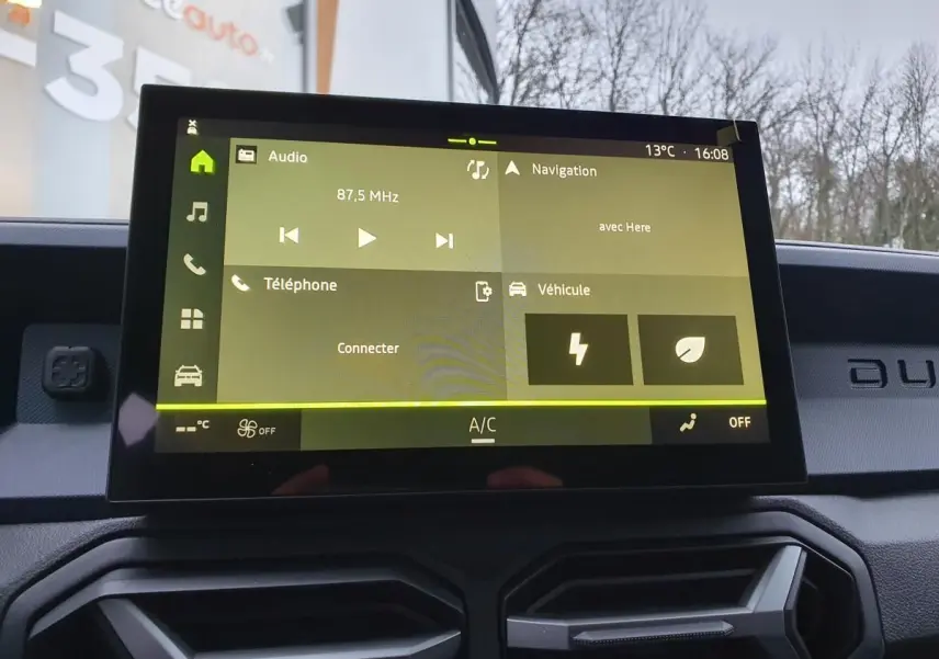 Écran tactile central du tableau de bord du Dacia Duster blanc glacier, affichant les menus audio et navigation.