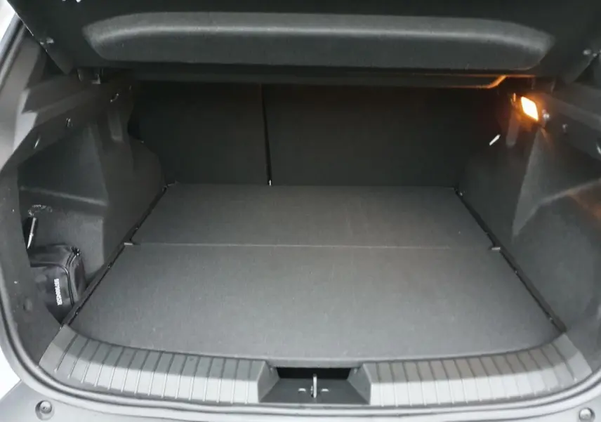 Coffre ouvert du Dacia Duster blanc glacier 2025, vue arrière montrant un espace de chargement plat et éclairé.