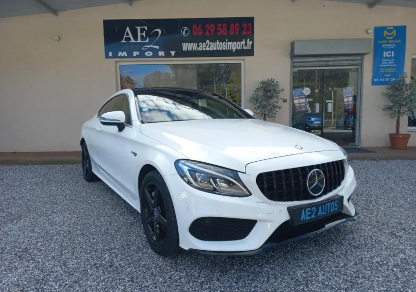 Vue 3/4 avant gauche d'une Mercedes Classe C Coupé blanche avec calandre noire et jantes noires, stationnée devant un garage.