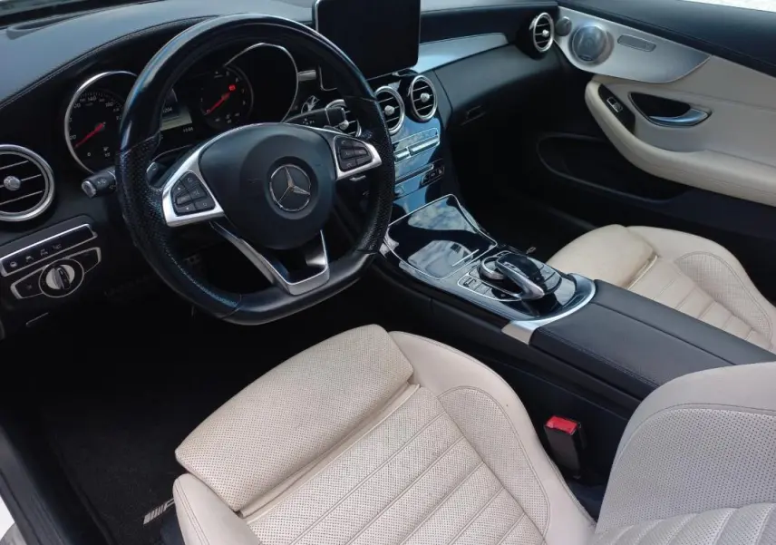 Vue intérieure côté conducteur de la Mercedes Classe C Coupé 2016, sièges cuir beige et tableau de bord noir brillant.