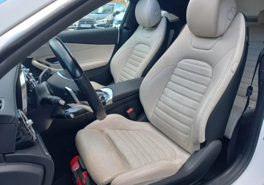 Vue intérieure côté conducteur d'une Mercedes Classe C Coupé 2016 avec sièges en cuir beige et volant multifonctions noir.
