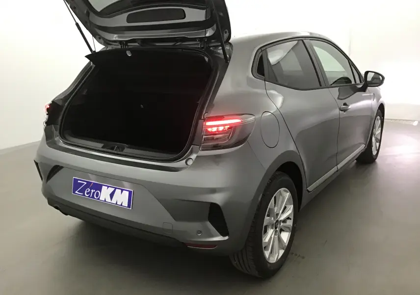 Vue 3/4 arrière droite d'une Renault Clio V gris schiste avec coffre ouvert et feux arrière allumés dans un studio.