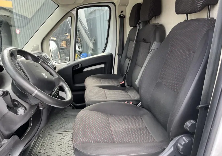 Vue intérieure côté conducteur du Peugeot Boxer Fourgon 2023, sièges tissu gris foncé avec motifs rouges.