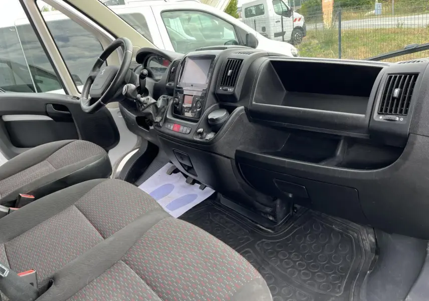Vue intérieure côté conducteur du Peugeot Boxer Fourgon 2023, tableau de bord noir et sièges tissu gris à motifs rouges.