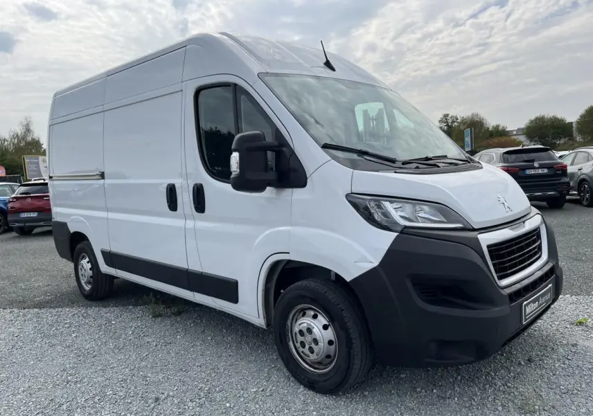 Fourgon utilitaire Peugeot Boxer blanc vu en 3/4 avant droit avec pare-chocs noirs et porte latérale coulissante.