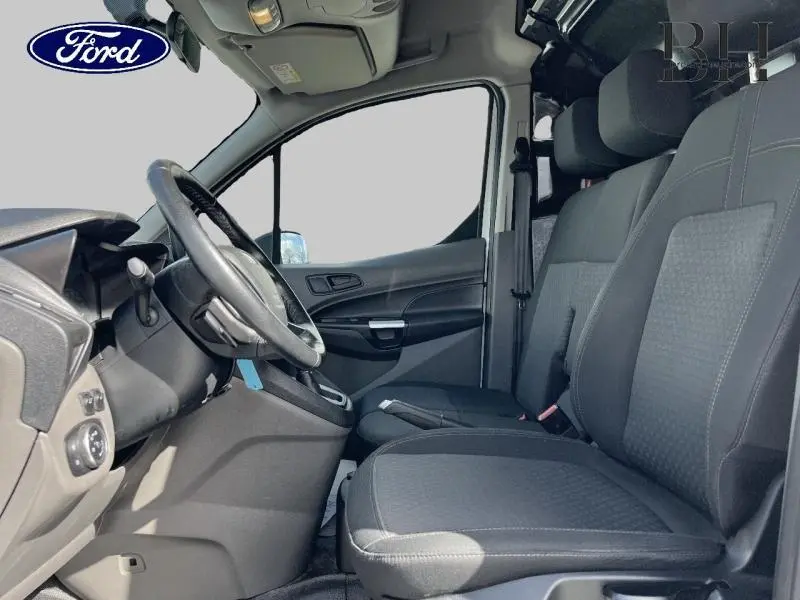Vue intérieure côté conducteur du Ford Transit Connect blanc glacier, montrant la banquette passagers et le volant multifonction.