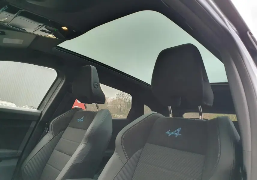 Vue intérieure des sièges avant en tissu carbone Alcantara gris avec logo Alpine bleu, toit panoramique en verre noir visible.