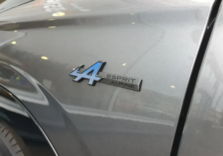 Gros plan sur l'emblème Esprit Alpine bleu sur l'aile avant droite d'un Renault Austral gris schiste.