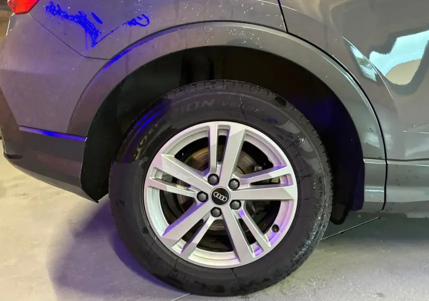Gros plan sur la roue arrière droite avec jante aluminium 17'' argent de l'Audi Q3 Sportback gris.