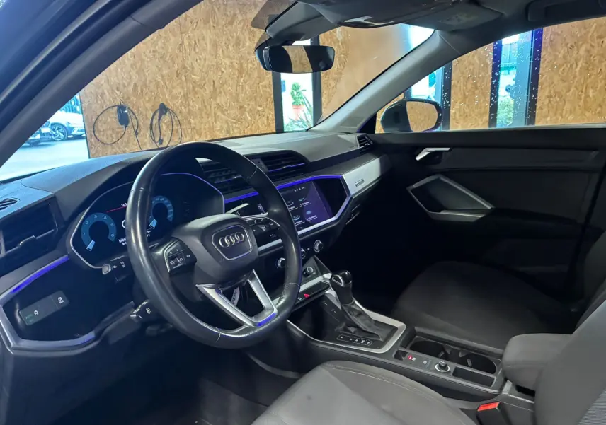 Vue intérieure côté conducteur de l'Audi Q3 Sportback gris, avec tableau de bord numérique et éclairage d'ambiance violet.