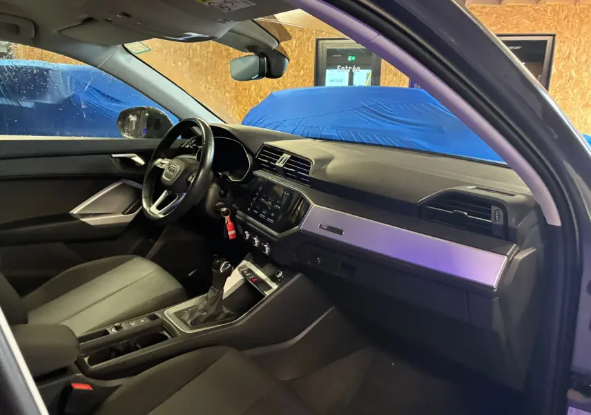 Vue intérieure côté conducteur de l'Audi Q3 Sportback gris, avec tableau de bord moderne et volant multifonctions cuir.