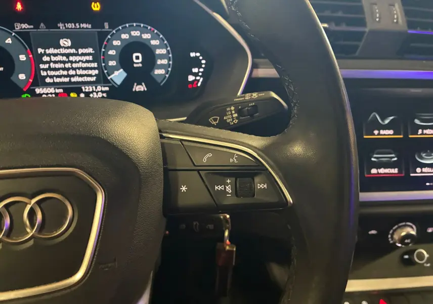 Gros plan sur le volant cuir multifonctions noir et tableau de bord numérique de l'Audi Q3 Sportback gris.