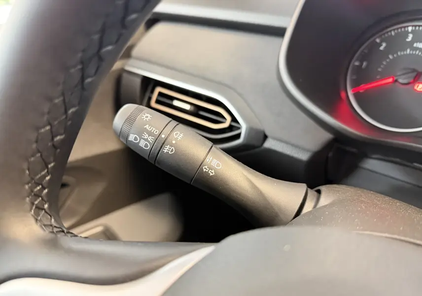 Gros plan sur la manette des feux et clignotants à gauche du volant dans l’habitacle noir du Dacia Jogger gris schiste.