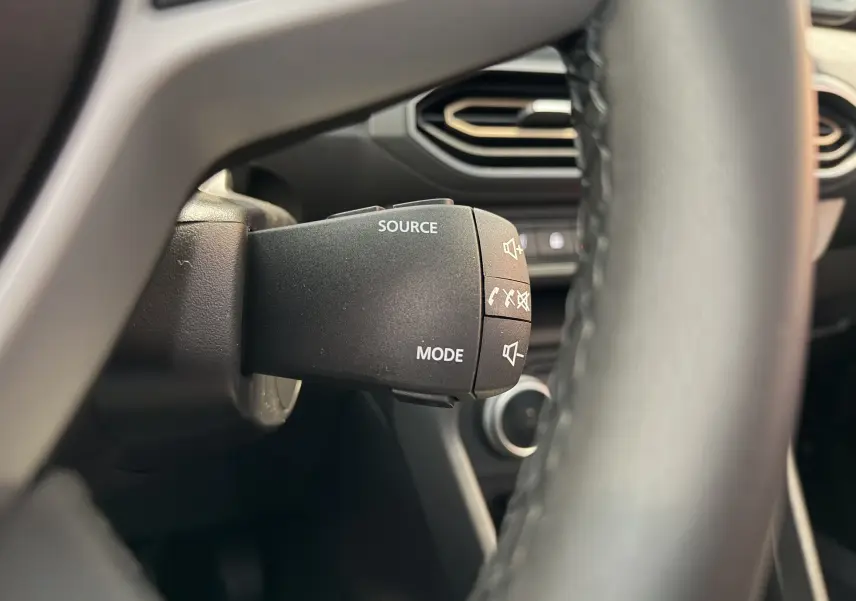 Gros plan sur la commande au volant du Dacia Jogger gris schiste, avec boutons source et mode visibles.