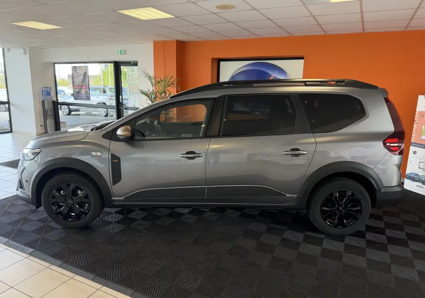 Vue latérale droite d'un Dacia Jogger gris schiste métallisé avec jantes noires, présenté en showroom.