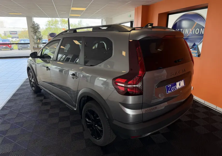 Vue 3/4 arrière droite d'un Dacia Jogger gris schiste métal avec jantes noires, stationné en intérieur showroom.