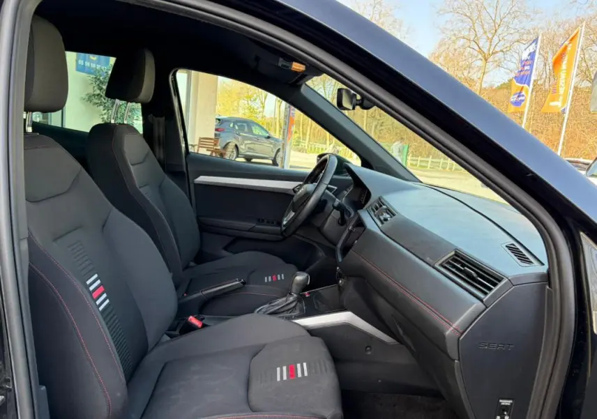 Vue intérieure côté conducteur du SEAT Arona noir 2020, montrant les sièges sport avec surpiqûres rouges et tableau de bord épuré.