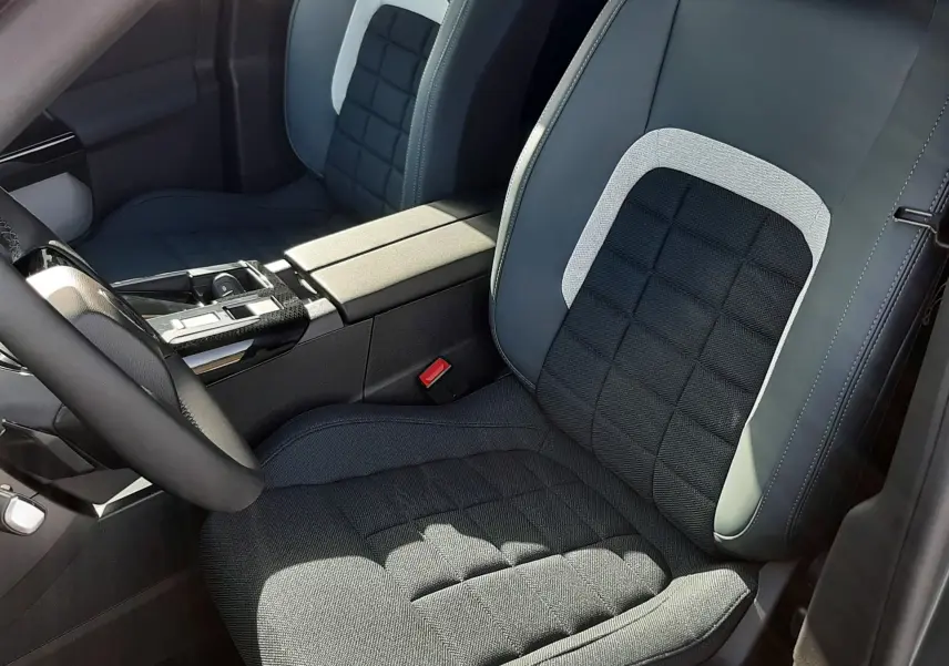 Vue intérieure rapprochée des sièges avant gris noir et tissu avec surpiqûres, console centrale et volant partiel visibles.