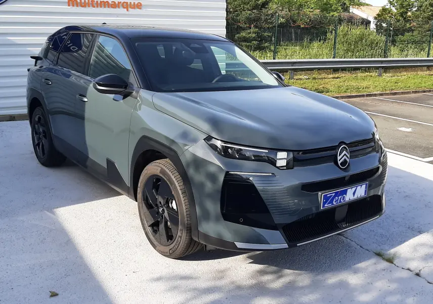 Vue 3/4 avant gauche d’un Citroën C5 Aircross 2026 vert Astoria avec toit noir et jantes noires, stationné devant un mur blanc.