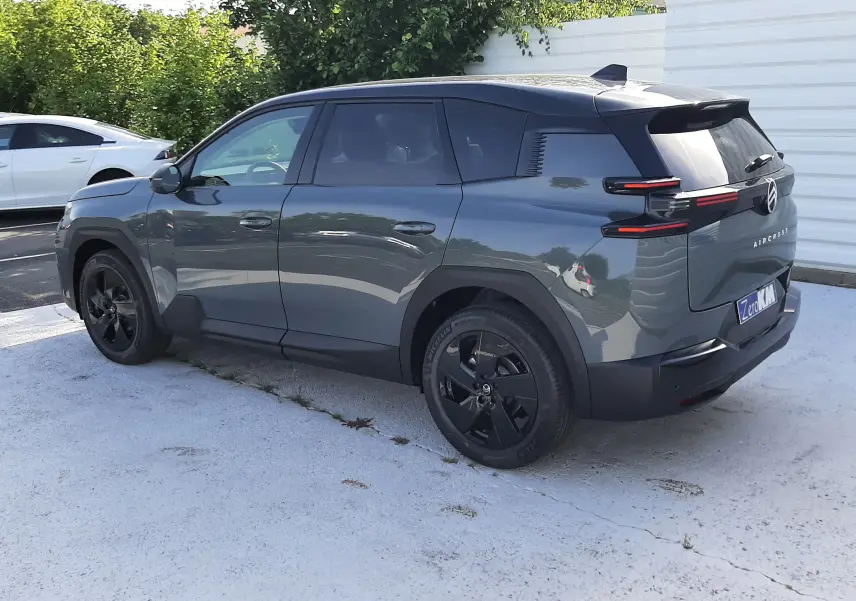 Vue 3/4 arrière droite d'un Citroën C5 Aircross vert Astoria avec toit noir et jantes noires, stationné en extérieur.