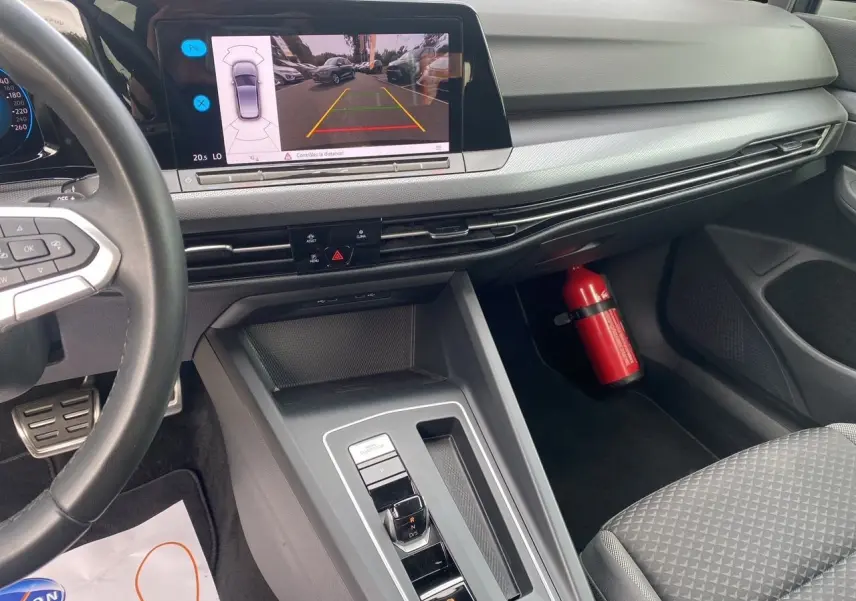 Intérieur noir de la Volkswagen Golf VIII, vue du tableau de bord et console centrale avec écran caméra de recul allumé.