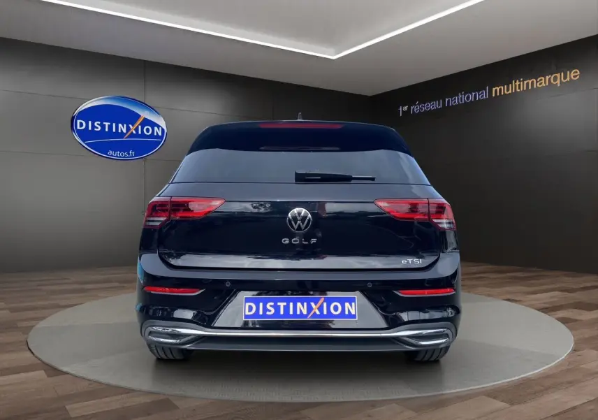 Vue arrière d'une Volkswagen Golf VIII noire avec logo et feux arrière allumés en showroom.