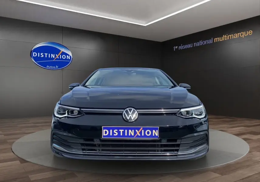 Vue frontale d'une Volkswagen Golf VIII noire, avec calandre et phares LED, dans un showroom Distinxion.