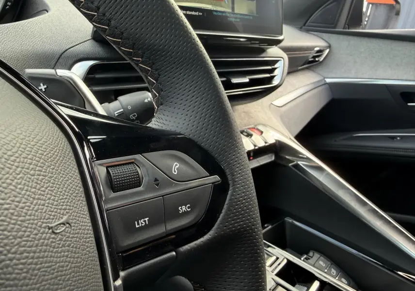 Gros plan sur le volant cuir perforé et la console centrale grise Alcantara du Peugeot 3008 Hybrid 2023.