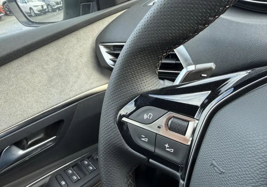 Gros plan sur le volant cuir perforé et la portière côté conducteur du Peugeot 3008 Hybrid gris, intérieur Alcantara.