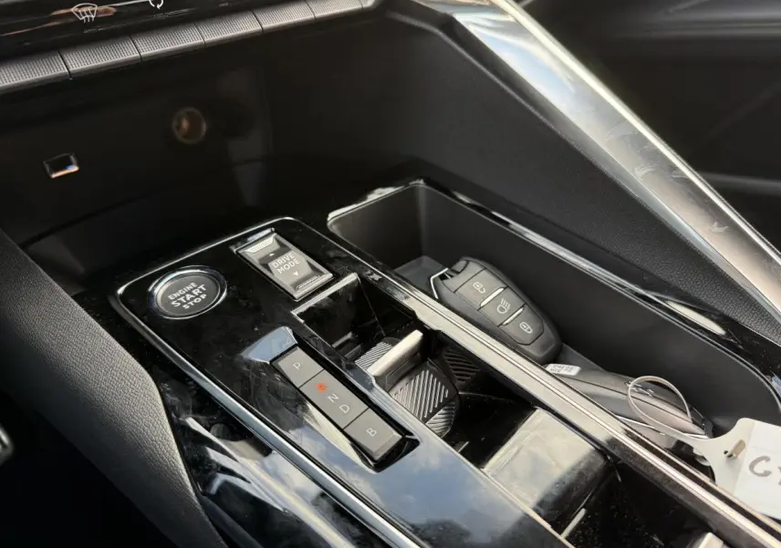Gros plan sur la console centrale noire brillante du Peugeot 3008 Hybrid 2023 avec bouton start, sélecteur de mode et clé électronique.