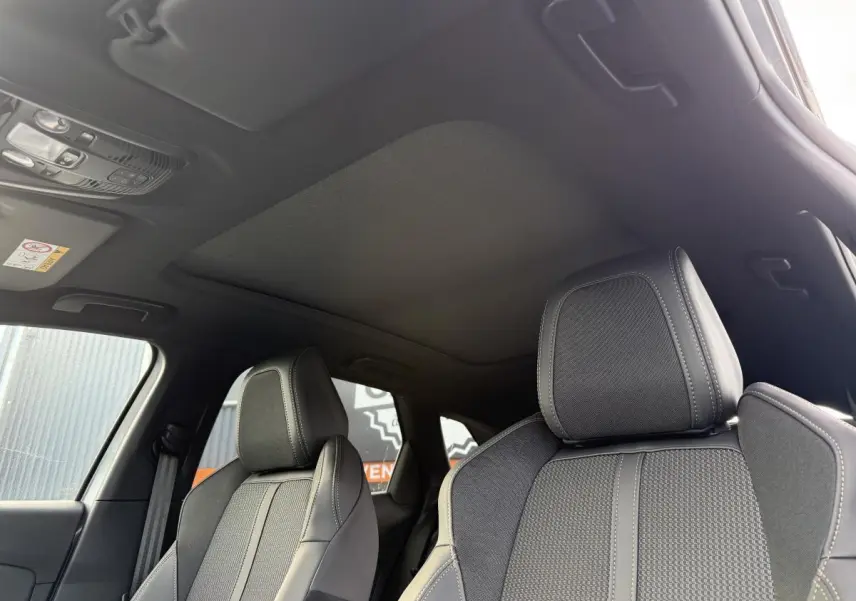 Détail intérieur montrant le toit ouvrant panoramique et les sièges avant gris du Peugeot 3008 Hybrid 2023.