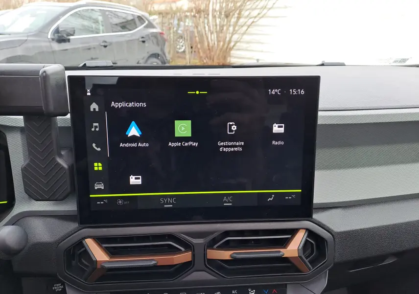 Vue intérieure du tableau de bord du Dacia Bigster 2025, écran tactile central avec applications et aérateurs noirs à inserts cuivrés.