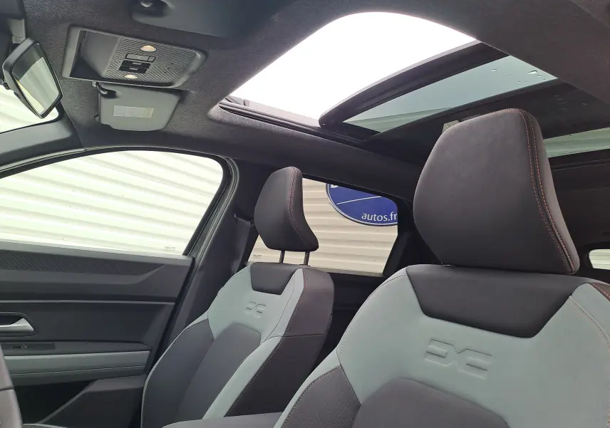 Vue intérieure avant du Dacia Bigster 2025, sièges gris et noirs avec surpiqûres orange et toit ouvrant panoramique.