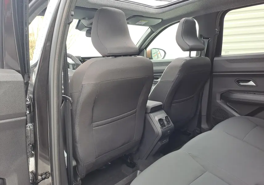 Vue intérieure arrière du Dacia Bigster noir nacré, montrant les sièges avant en tissu gris et les aérateurs centraux.