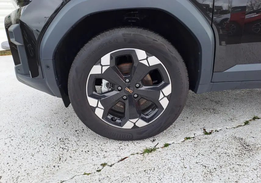 Gros plan sur la roue avant gauche du Dacia Bigster noir nacré, mettant en valeur la jante bi-ton au design géométrique.