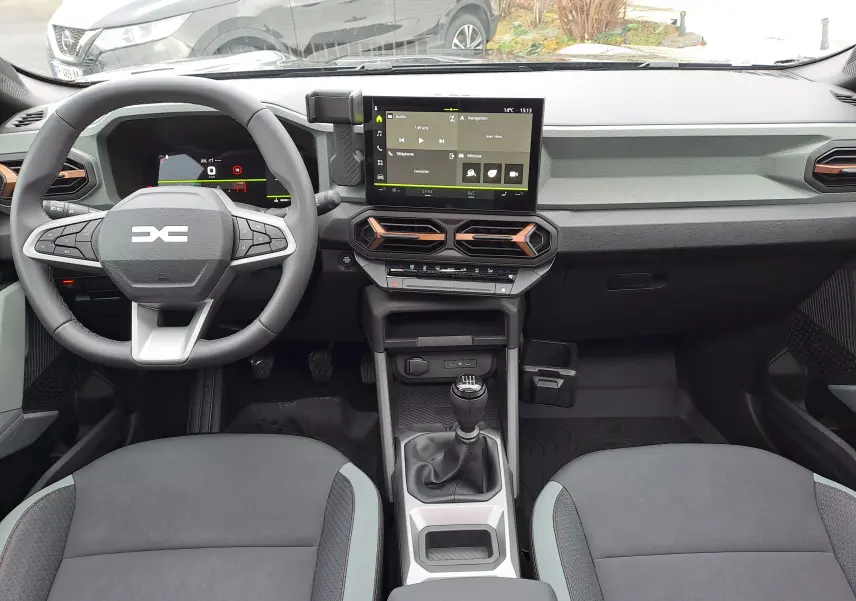Vue intérieure frontale du tableau de bord et volant du Dacia Bigster 2025, avec écran tactile et levier de vitesses manuel.