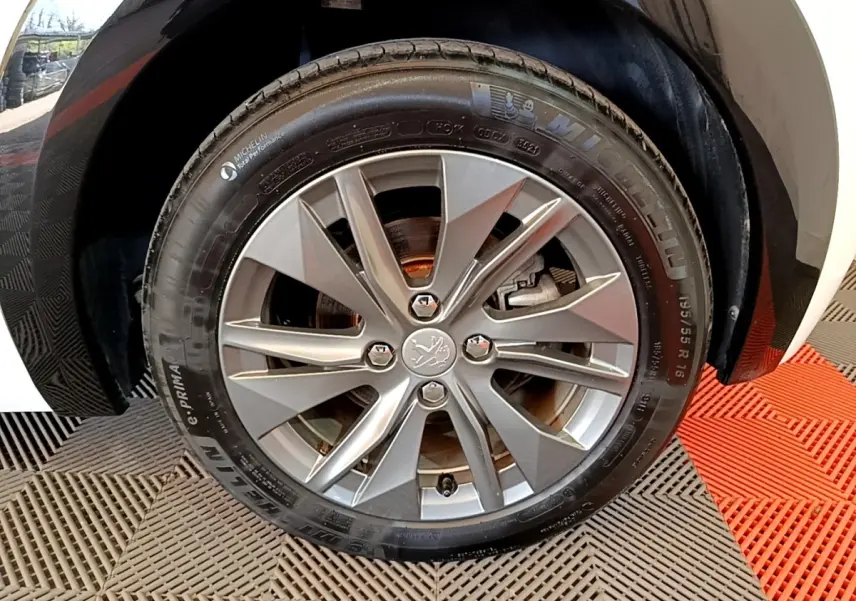 Gros plan sur la roue arrière droite d'une Peugeot 208 électrique blanche, avec partie de la carrosserie visible.