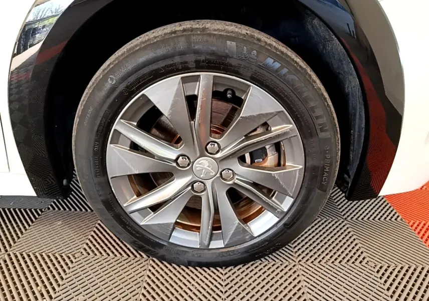 Gros plan sur la roue avant droite d'une Peugeot 208 électrique blanche, jante alliage à cinq doubles branches.