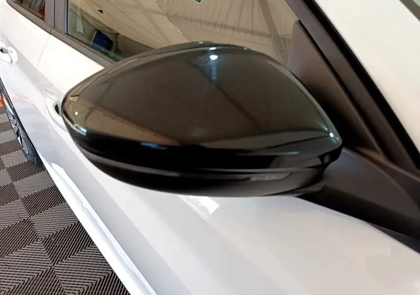 Gros plan sur le rétroviseur noir côté droit d'une Peugeot 208 électrique blanche, vue partielle latérale.