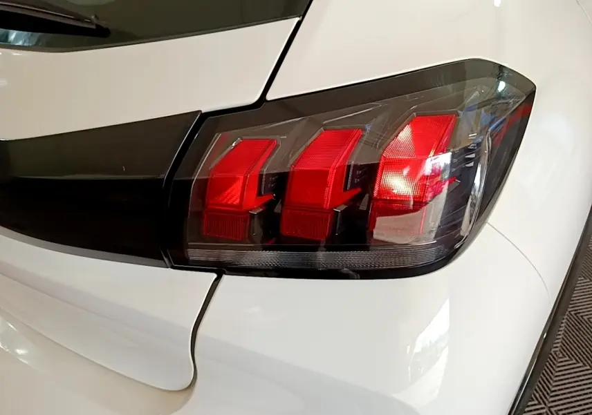 Gros plan sur le feu arrière droit rouge d’une Peugeot 208 électrique blanche, avec partie arrière visible.