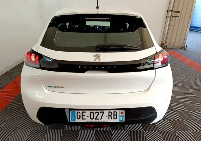 Vue arrière d'une Peugeot 208 électrique blanche avec bande noire et feux arrière allumés en intérieur.