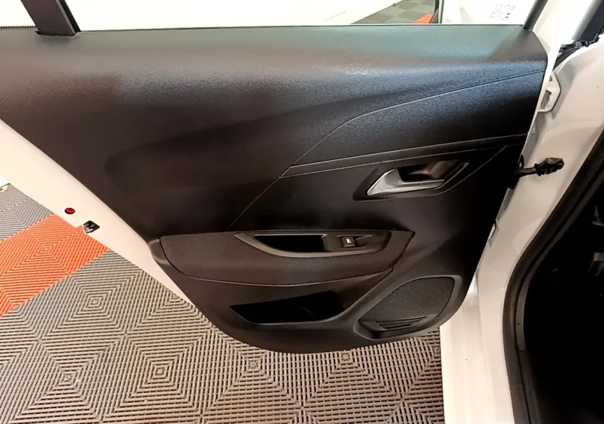 Vue intérieure sur la porte arrière droite noire d’une Peugeot 208 électrique blanche de 2022, avec poignée et commande vitre.