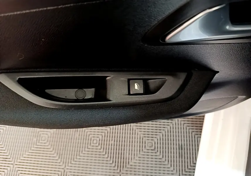 Détail de la commande de lève-vitre côté conducteur sur la porte intérieure d’une Peugeot 208 électrique blanche.